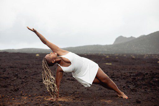 A woman in white doing yoga on top of a hill.